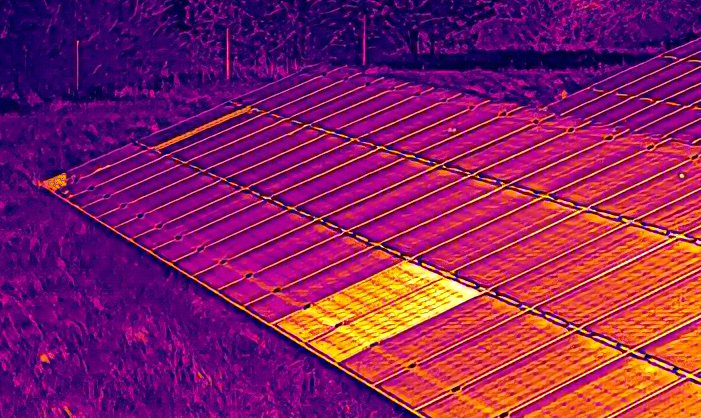 Das Bild zeigt eine PV-Freiflächenanlage im Wärmebild bei der Drohneninspektion. Vorne rechts sind 2 Module sehr hell. Diese Module können offensichtlich keine Energie in die Verkabelung abgeben und werden daher sehr warm. Dem Betreiber entgehen durch nicht funktionierende Module über die Dauer erhebliche Gewinne. Regelmäßige Solar-PV-Checks sichern die geplanten Erträge.