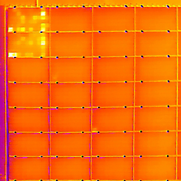 Das Bild zeigt ein PV-Dach im Wärmebild bei der Drohneninspektion. Die 2 PV-Modulflächen oben links zeigen auffällige weiße Quadratflächen. Dies sind heiße Photovoltaik-Zellen, sogenannte Hotspots. Da es keine Vermutzungen oder Verschattung auf den Hotspots gibt, ist eine Beschädigung der 2 Module sehr wahrscheinlich.